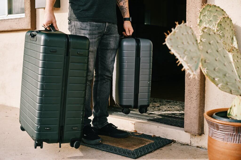 waist down photo of a man holding two suitcases outside of his front door