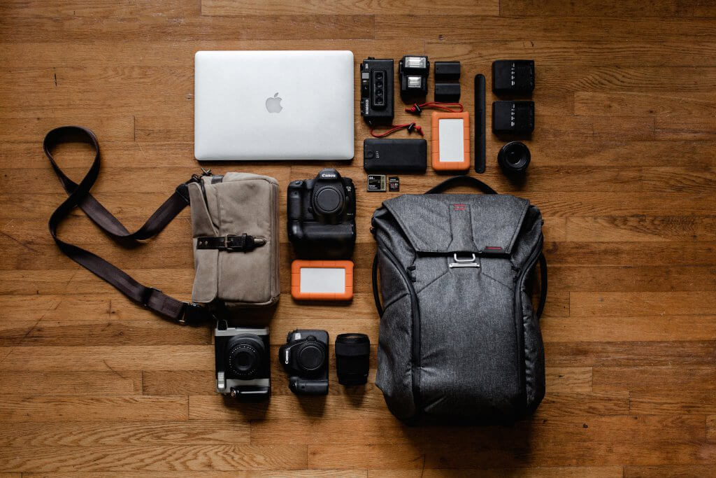 flat lay of a laptop, cameras, hard drives, and a backpack