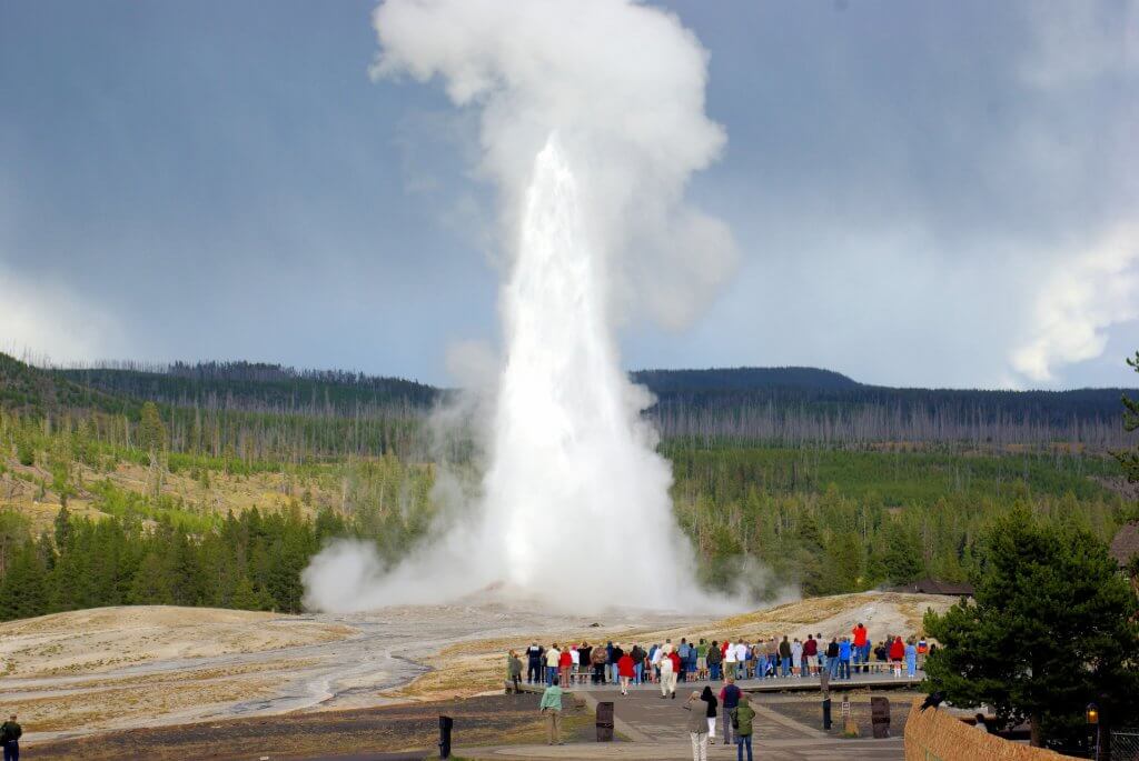 people gathering on a boardwalk as Old Faithful Geyser erupts in yellowstone national park