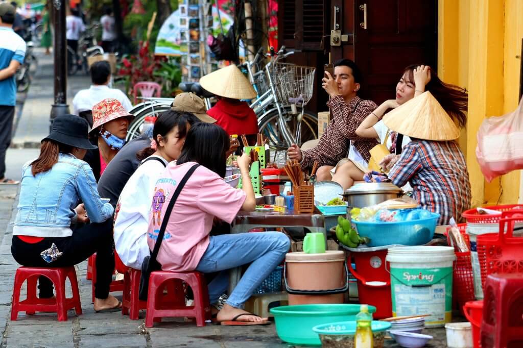 women sitting on a sidewalk while eating in Hanoi Vietnam