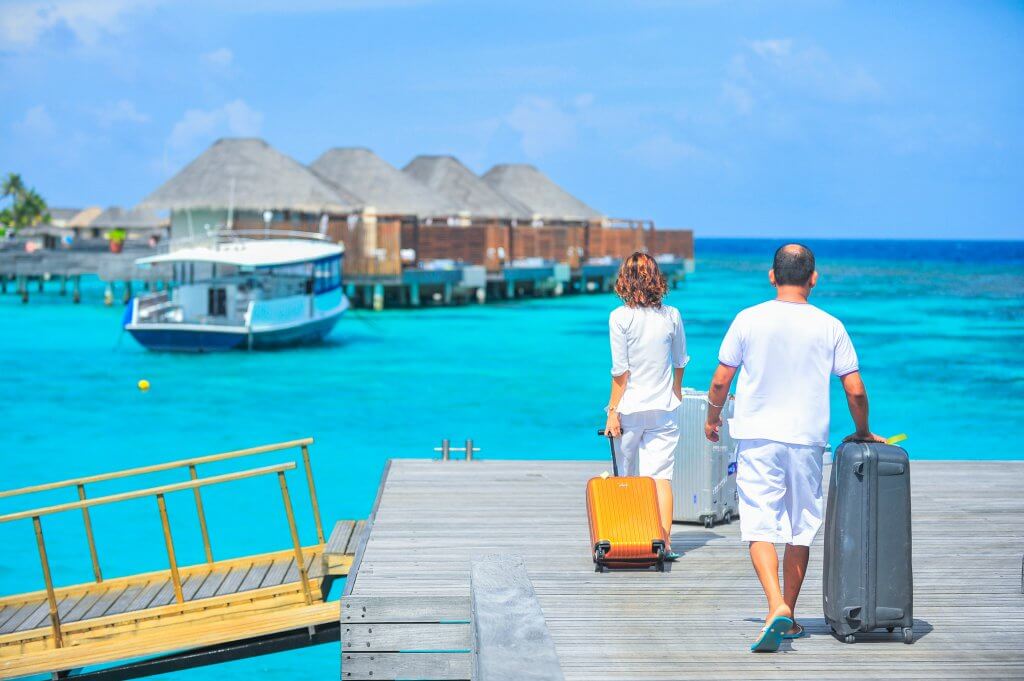 couple on a romantic getaway pulling suitcases toward over water bungalows