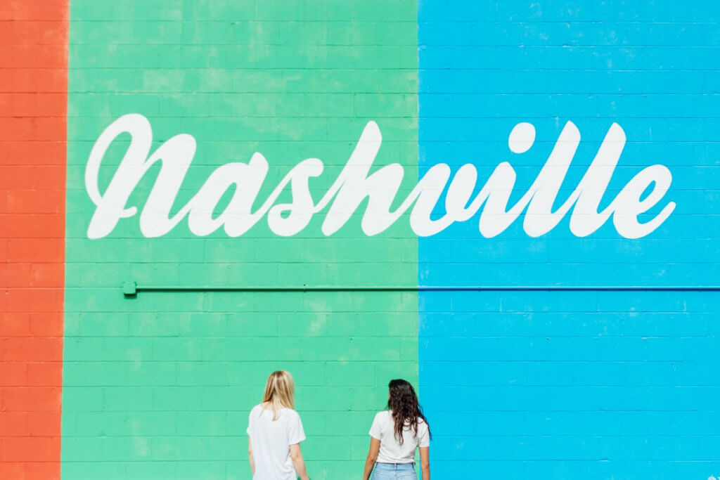 two women stand with their backs to the camera facing a mural that says "nashville"