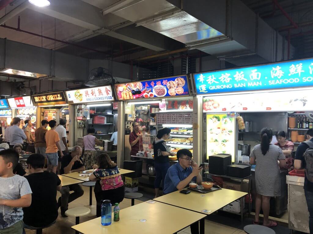 people sit in front of food stalls at Singapore's old airport road hawker center