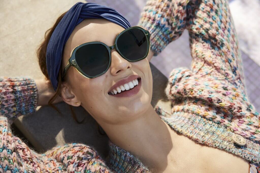 smiling woman laying down with her hands behind her head wearing sunglasses