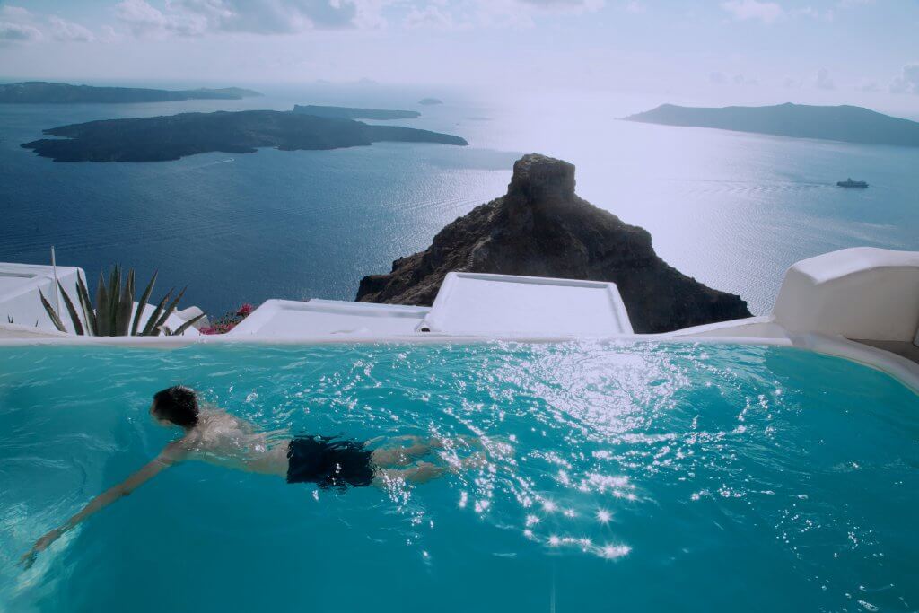 man swimming in a pool with an ocean view in santorini