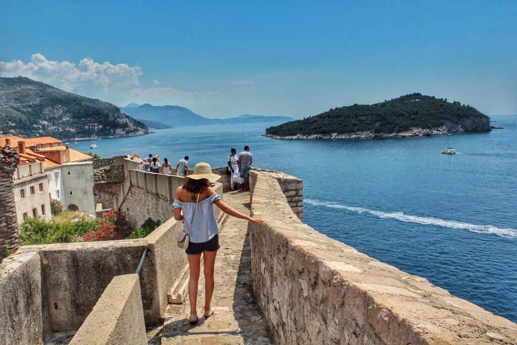 woman walking along Dubrovnik's old city walls while looking out over the sea