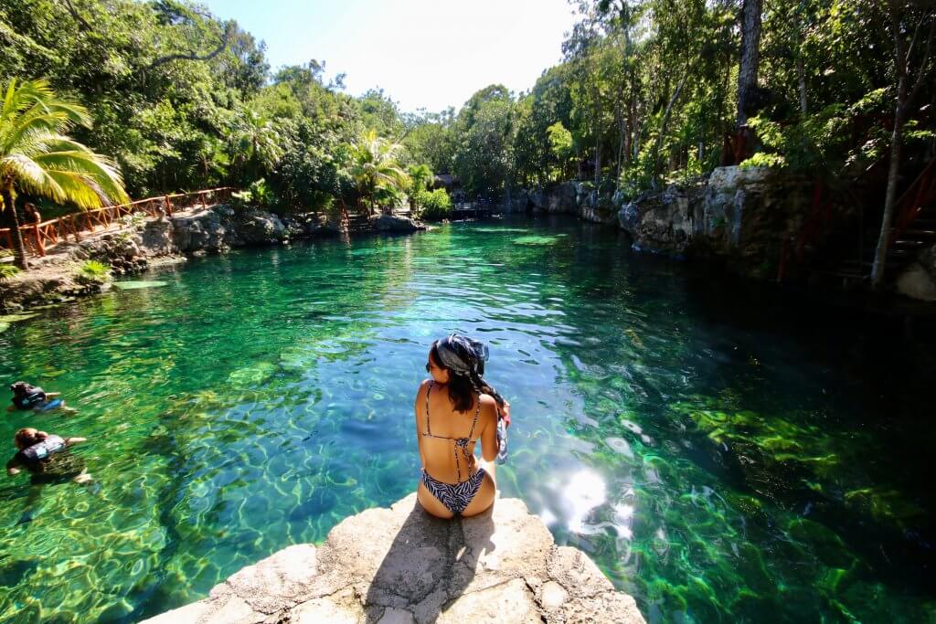woman sits on a rock overlooking a cenote near Tulum, Mexico